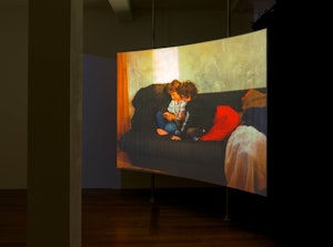 A curved screen suspended from the ceiling shows an image of two children on a sofa examining a phone.