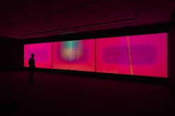Three bright pink screens in a darkened gallery