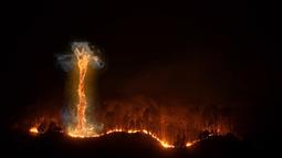 A stretch of forest is engulfed in flames, a towering fire tornado swirls amongst the burning trees.