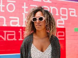 A person wearing pink sunglasses standing against a pink and red painted background