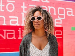 A person wearing pink sunglasses standing against a pink and red painted background
