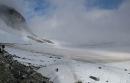 Taken from high up this image shows two people who are small in the distance standing upon icy landscape, in front of them is icy wind