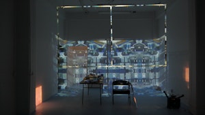 In a dark gallery images are projected onto a table and chairs against a wall