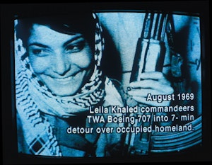 A woman is smiling, holding a gun on a grainy tv. Text on top of the images reads, "August 1969. Leila Khled commandeers TWA Boeing 7070 into 7-min detour over occupied homeland."