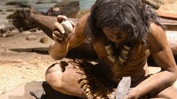 A museum model of an indigenous ancestor sitting down holding a rock in each hand.