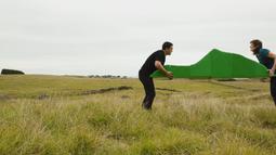 In a large field two people carry a green sculpture of a hill.