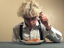 A person wearing a white shirt and suspenders sits at a table eating spaghetti.