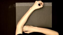 A Birds Eye view of someone writing with a white pencil on black paper.