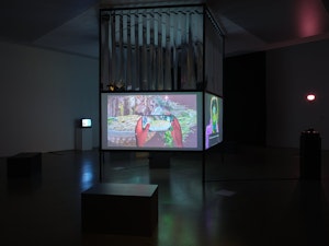 Installation view of a two-sided screen structure showing Sorawit Songsataya's video work in a darkened room.