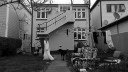 A person wearing a white sheet looks at a dog while standing in a backyard. There are chairs and a couch on the lawn.