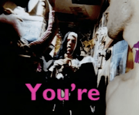 In a cluttered hallway, a person dances in front of a man dressed as a nun. He closes his eyes and opens his mouth slightly. Large pink text or subtitles reads "you're"