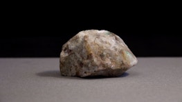 A close up of a brain shaped rock. The rock is cream coloured with green and yellow details, it has a crystal like texture.