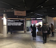 People move through a gallery space with concrete floors. Signage reads "riding hall galleries"