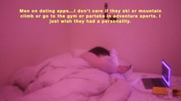 A  person lies in bed with an open laptop beside them while they're on their phone. The room is in pink light.