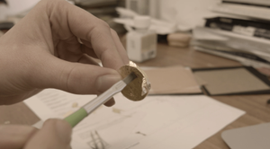 Gold leaf is being pushed lightly by a paintbrush onto a coin shape making counterfeit gold coin