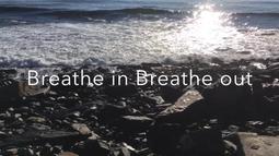 In low sunlight a small waves breaks on rocks. Over the top is the text 'Breathe in Breathe out'.