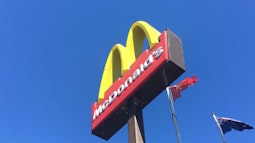 A McDonald's sign as seen from below, with deep blue sky above. The New Zealand flag flies beside it.