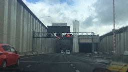 The view from the front seat of a car as it drives towards a large urban tunnel.