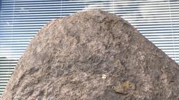 A rock sits in front of a window with it's blinds down.