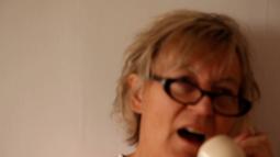 An out of focus woman wearing black glasses talks into a phone.