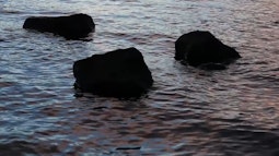 Three rocks stick out above the water in dim evening light.