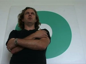 Julian stands with his arms folded looking serious infront of a green circular painting