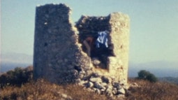 A person climbs inside an old rock fort, a blue shirt hangs on the edge.
