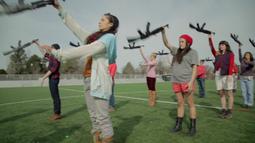 A group of people stand in lines on a field practicing manoeuvres with rifles.