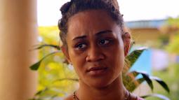 A close up of a woman looking out of frame. Leaves from plant appear behind her.