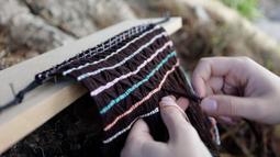 A close up of a weaving being made, the top edge is nailed in place to a plank of wood.