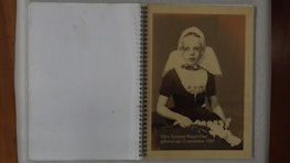 An open phot album showing a young Dutch girl in 1909 wearing ornate and proper dress for the camera