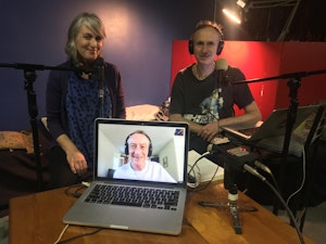 Stella Brennan and Mark Amergy smile in a audio studio holding a laptop showing Sean Cubitt smiling