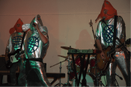 Three people perform music wearing shiny silver costumes and fish masks