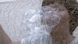 A person blows bubbles through mesh fabric.