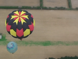 Hot air balloons rise over bare fields