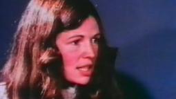 A woman sits talking to someone off frame.