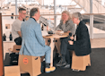 Four people sit around a small table at the airport, having a discussion