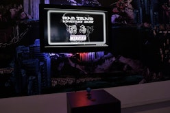 A video game called Brain Island is displayed on an LCD monitor. In front is a blue joystick. Behind the monitor is a series of digital images from the game which are high gloss but whose content indistinct