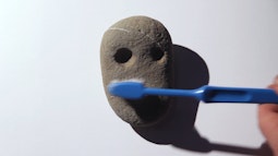 A rock with two cut outs resembling eyes is brushed with a toothbrush.