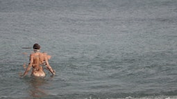 A person wades into the sea naked, their body becoming increasingly pixelated and distorted.