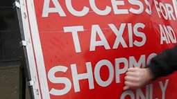 A fist hits a bight red sign that has the text "Access for taxis and shop..." some of the text is obscured.