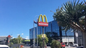 On a bright day in a city McDonald's signage of illuminated golden arches guides customers to the drive-thru