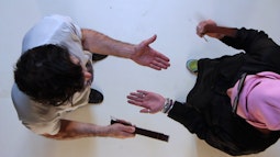 A birds-eye view of two people as they stand using straps to slap each-others open palms.