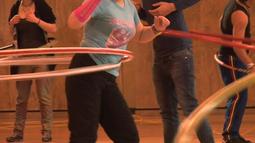 In a gymnasium a group of people practice using hula hoops.