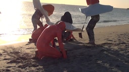 A group of people wearing inflatable plastic outfits perform on a beach at sunset.