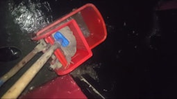 A handheld view of someone mopping a black floor, the bucket is bright red.