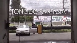 In a car garage a person stands by the open door of a white car. The text "Tongdo Fantasia" is written onscreen.