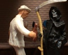 A model of a person in a white hat and suit is talking to a model of the grim reaper