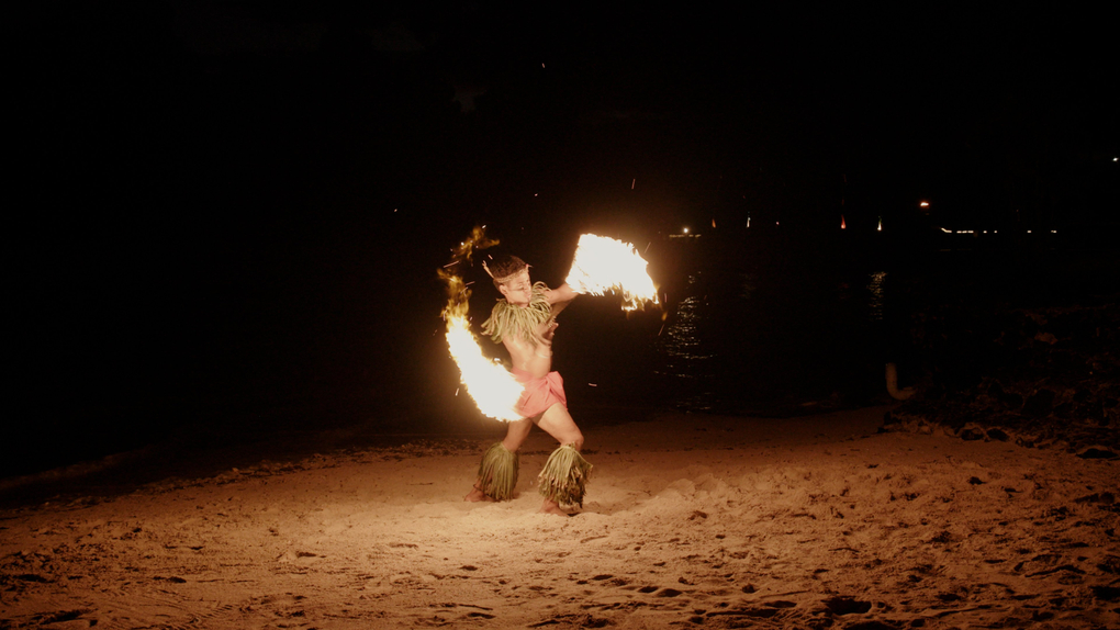 A performer spins a nifo oti (fire knife) on the beach at night