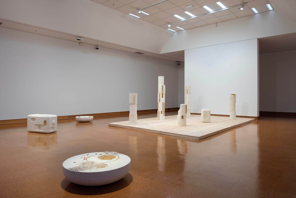 Installation view of a gallery with cork floors and various column-like stone sculptures.